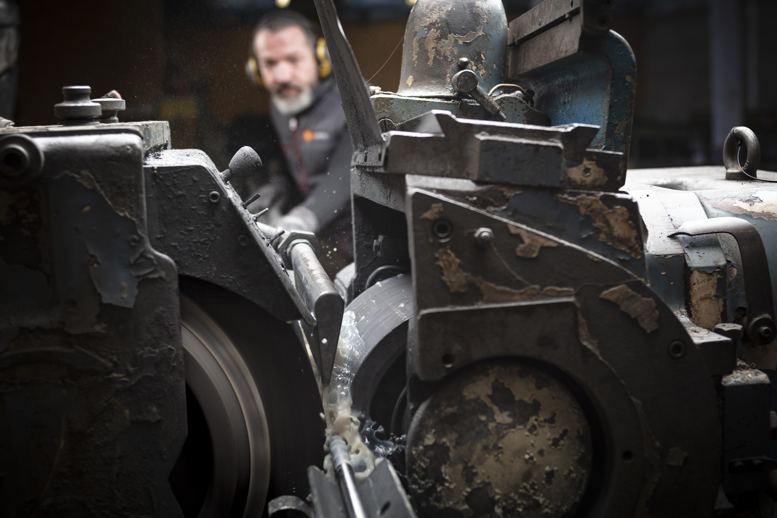 Machine de rectification centerless en fonctionnement — barre métallique entre les meules, lubrification en cours